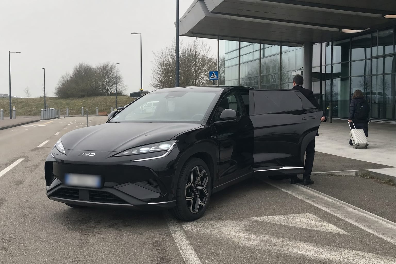 Le BYD Sealion 7 noir de VTC G à la dépose minute d’un terminal d’aéroport, chauffeur à la portière