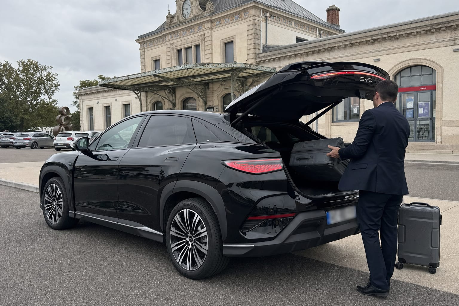 Chauffeur VTC G chargeant les valises dans le coffre du SUV électrique noir, devant une gare